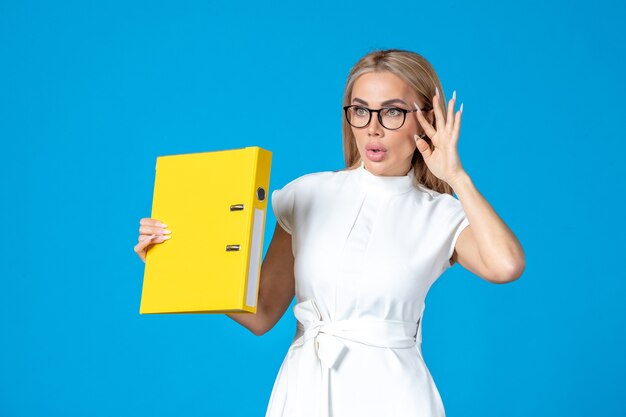 Free photo front view of female worker in white dress holding yellow folder on blue wall