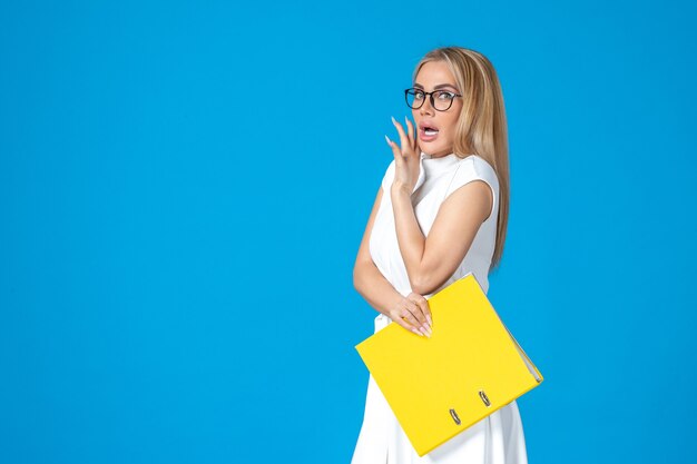 Front view of female worker in white dress holding yellow folder on blue wall