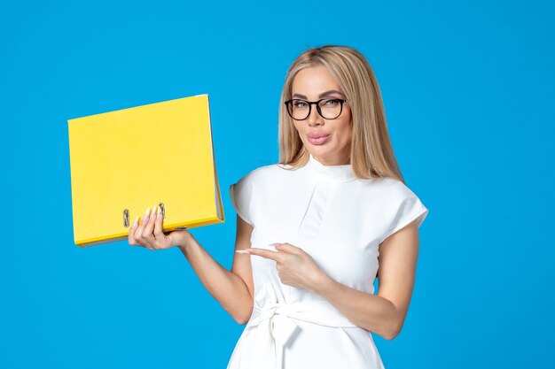 Front view of female worker in white dress holding yellow folder on blue wall