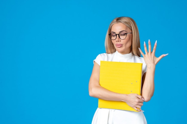 Front view of female worker in white dress holding yellow folder on blue wall