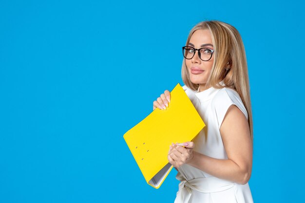 Front view of female worker in white dress holding yellow folder on blue wall