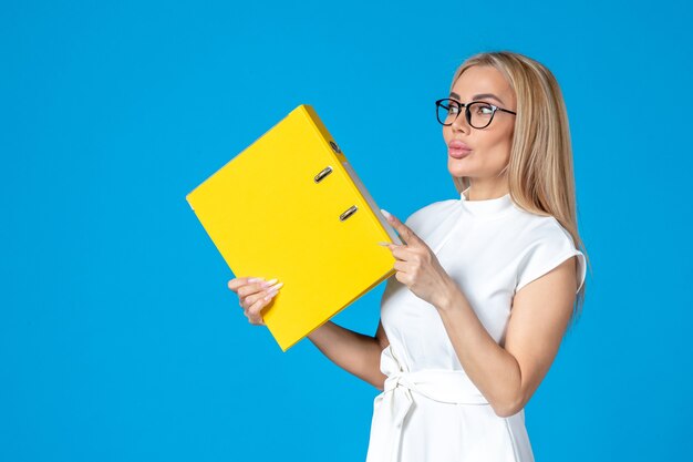 Front view of female worker in white dress holding yellow folder on blue wall