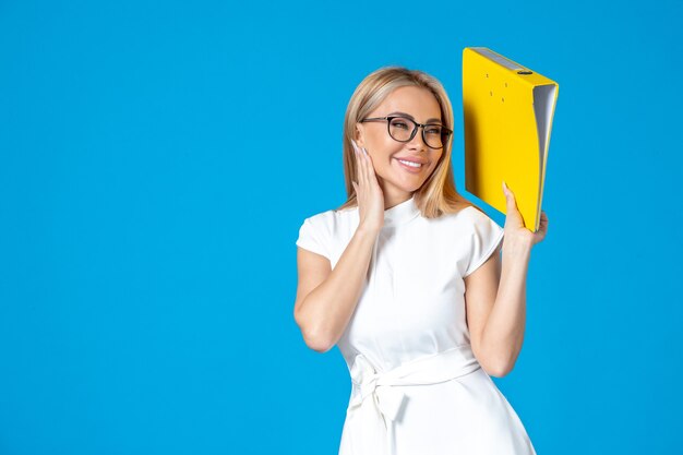 Front view of female worker in white dress holding yellow folder on blue wall