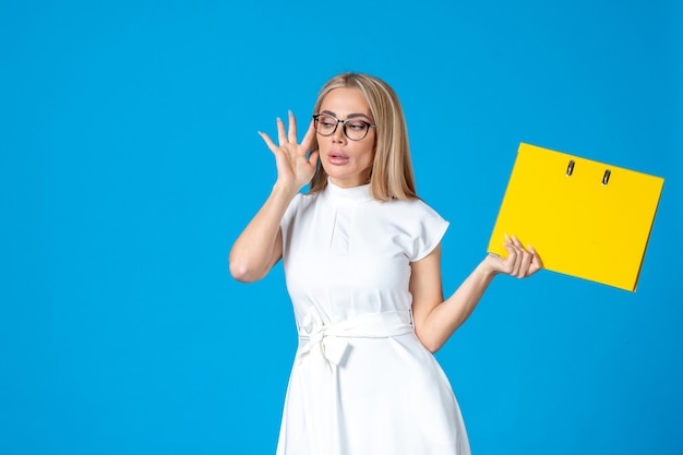 Front view of female worker in white dress holding yellow folder on blue wall