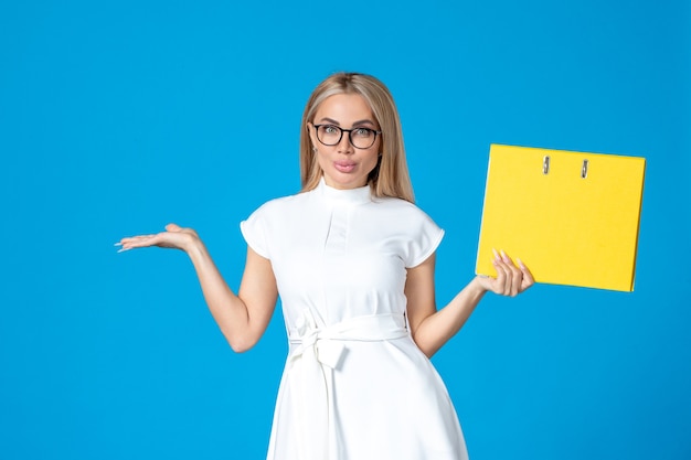 Front view of female worker in white dress holding yellow folder on blue wall