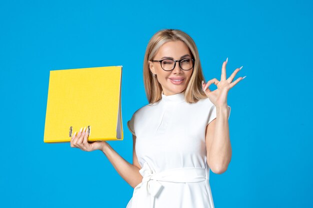 Front view of female worker in white dress holding yellow folder on blue wall