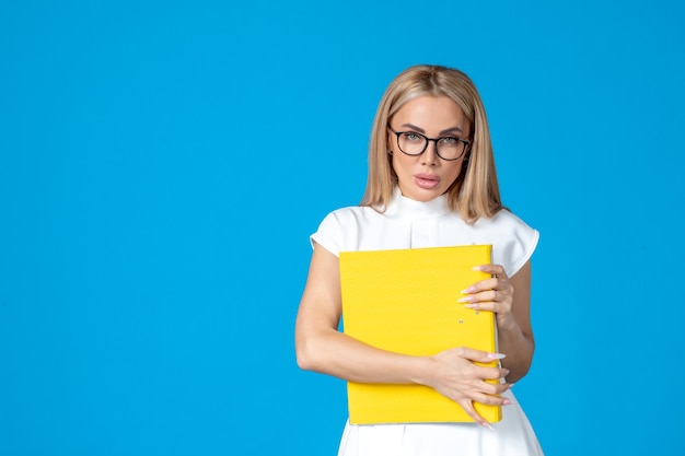 Front view of female worker in white dress holding yellow folder on blue wall