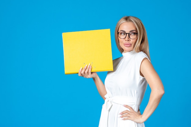 Front view of female worker in white dress holding yellow folder on blue wall