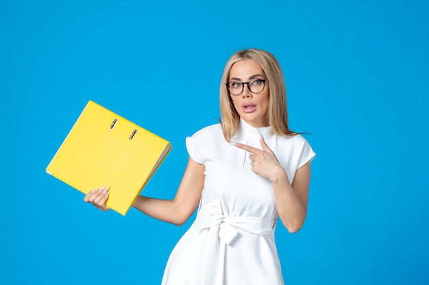 Front view of female worker in white dress holding yellow folder on blue wall