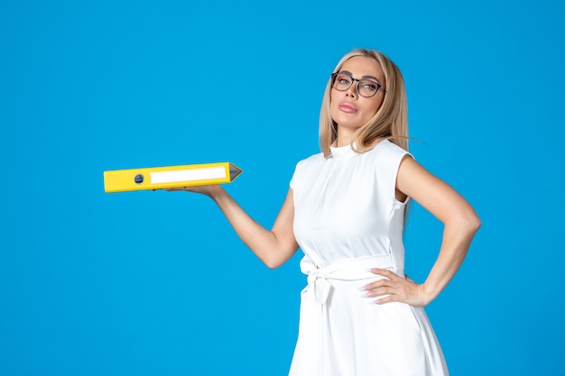 Front view of female worker in white dress holding yellow folder on blue wall