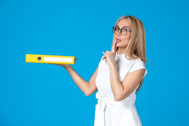 Front view of female worker in white dress holding yellow folder on blue wall