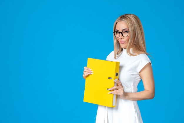 Free photo front view of female worker in white dress holding yellow folder on blue wall