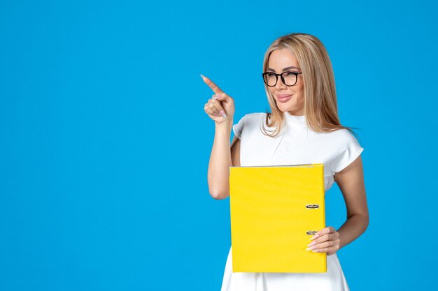 Front view of female worker in white dress holding yellow folder on blue wall