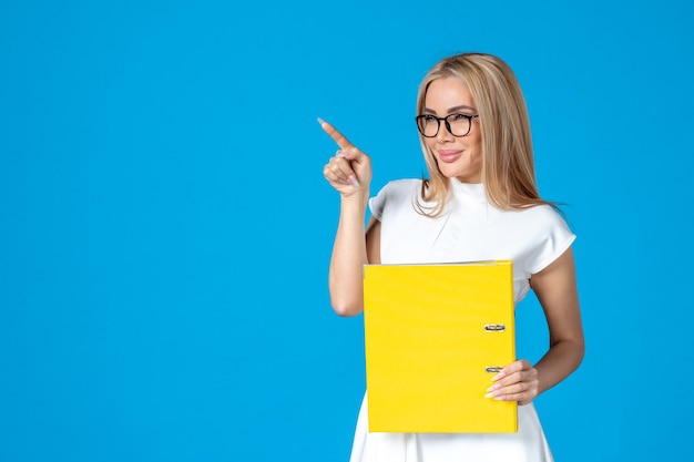 Front view of female worker in white dress holding yellow folder on blue wall