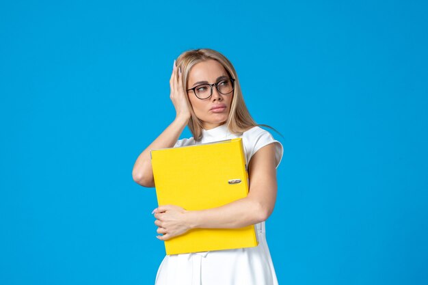 Front view of female worker in white dress holding yellow folder on blue wall