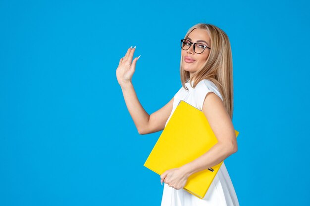 Front view of female worker in white dress holding yellow folder on blue wall