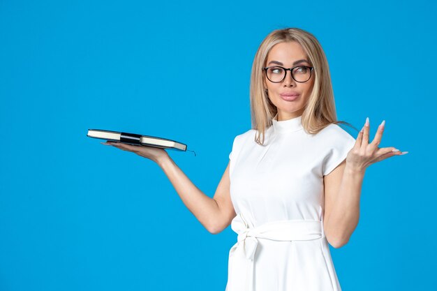 Front view of female worker in white dress posing with notepad on blue wall