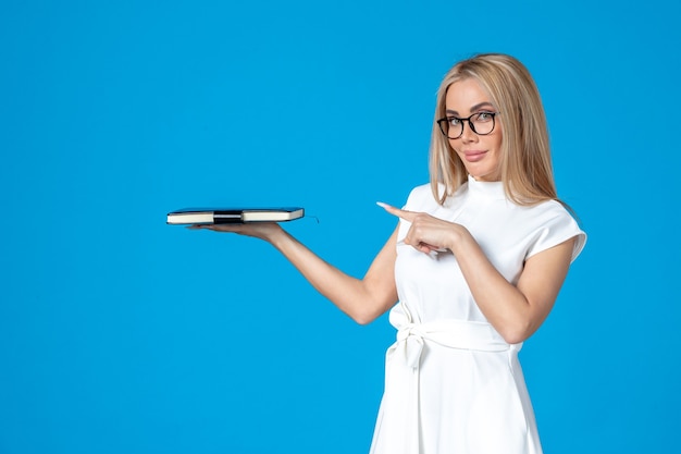 Front view of female worker in white dress posing with notepad on blue wall