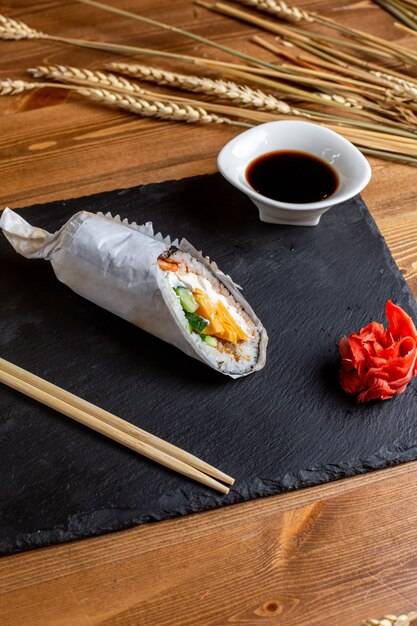 A front view fish rolls filled with sliced vegetables rice along with black sauce meal fish japan