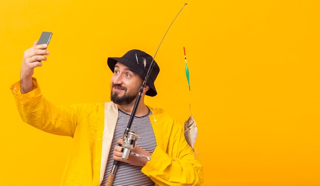 Front view of fisherman holding fishing rod and taking selfie