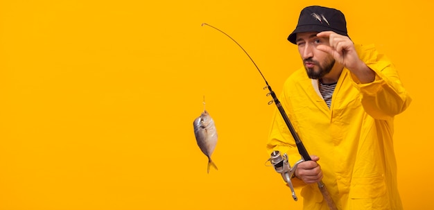 Front view of fisherman holding fishing rod with catch and copy space