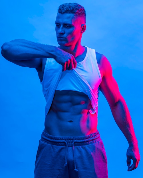 Front view of fit man posing while lifting tank top