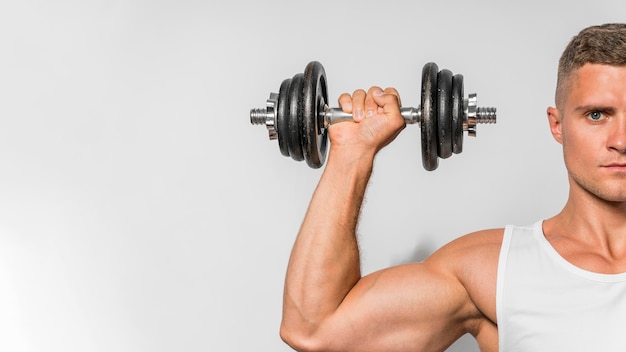 Front view of fit man with tank top holding up weights with copy space