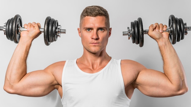 Front view of fit man with tank top holding up weights