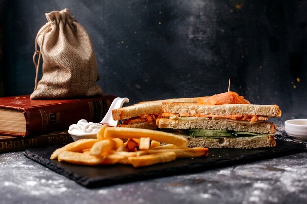 Front view french fries along with sandwiches on the black desk and grey surface