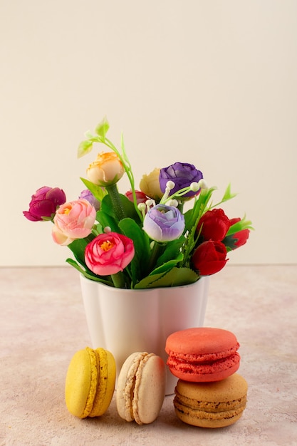 Foto gratuita una vista frontale macarons francesi deliziosi con fiori sulla scrivania rosa