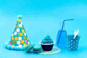 Foto gratuita una vista frontale macarons francesi con blu, bevanda da dessert e berretto di compleanno su blu, compleanno festa di celebrazione