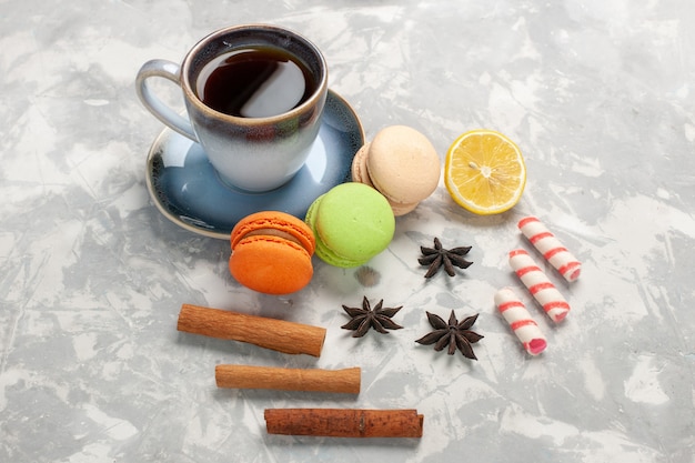 Foto gratuita macarons francesi di vista frontale con la tazza di tè sul biscotto dolce della torta di zucchero della torta di superficie bianca