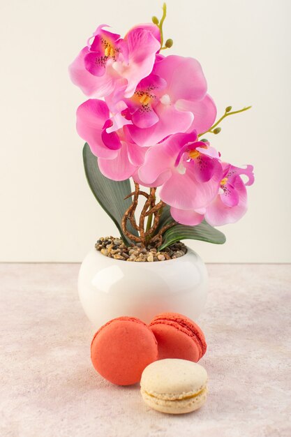 ピンクの机の上の花を持つ正面フレンチマカロン