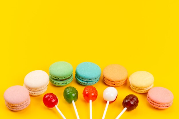 A front view french macarons with lollipops on yellow, sugar candy cake