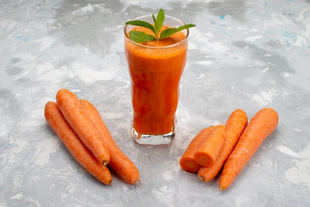 Свежий морковный сок, вид спереди, в длинном стакане с листьями и здоровыми овощами из свежей моркови
