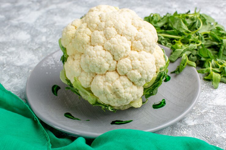 Front view of fresh cauliflower with greens on the grey desk