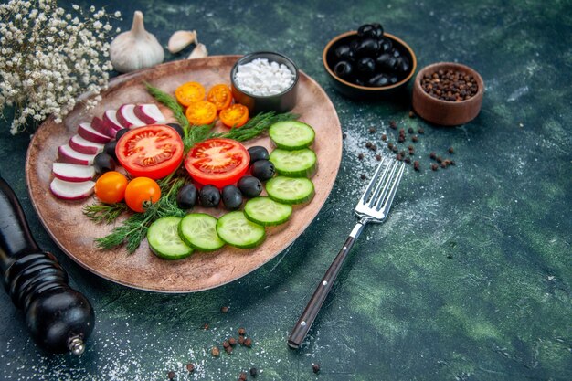 Front view of fresh chopped vegetables olives salt in a brown plate and kitchen hammer garlics flower on green black mixed colors background