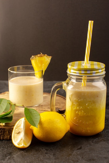 A front view fresh cocktail yummy cooling drink inside can with straw near wooden desk along with green leaves on the dark background drink summer juice