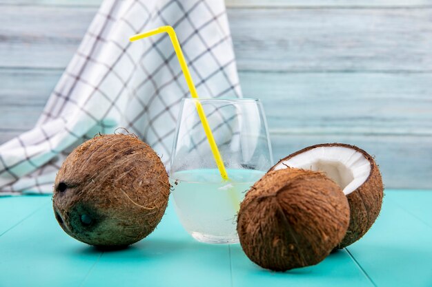 Front view of fresh coconuts with a glass of water on tablecloth and grey wooden surface