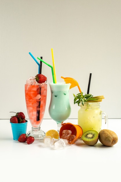 A front view fresh cold cocktails inside glasses with straws along with fresh fruits isolated on white