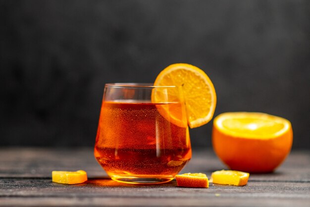 暗い背景にオレンジ色のライムとガラスの新鮮なおいしいジュースの正面図
