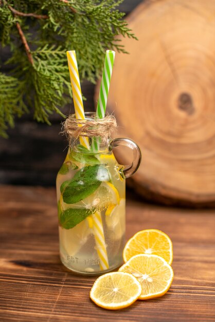 Вид спереди свежей воды для детоксикации в стакане с трубками и лимонным лаймом на деревянном столе
