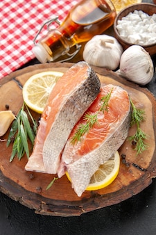 Вид спереди кусочки свежей рыбы с ломтиками лимона, чесноком и приправами на темном блюде из морепродуктов цветная еда мясо фото сырое
