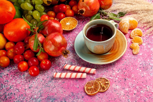 淡いピンクの机の上のお茶と正面図の新鮮な果物の組成