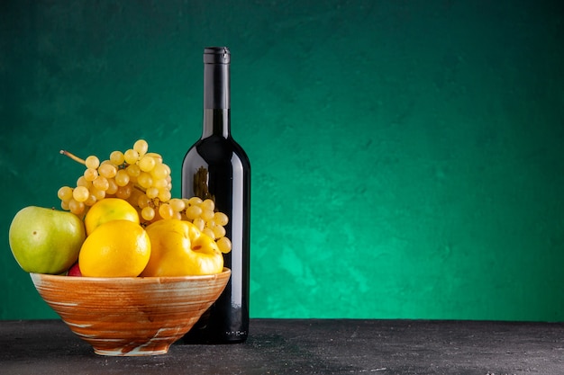 Front view fresh fruits in wooden bowl apples quince lemon yellow grapes wine bottle on green table free space