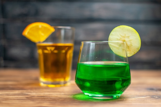 Free photo front view fresh fruity juice orange and apple drinks inside glasses on a brown wooden desk