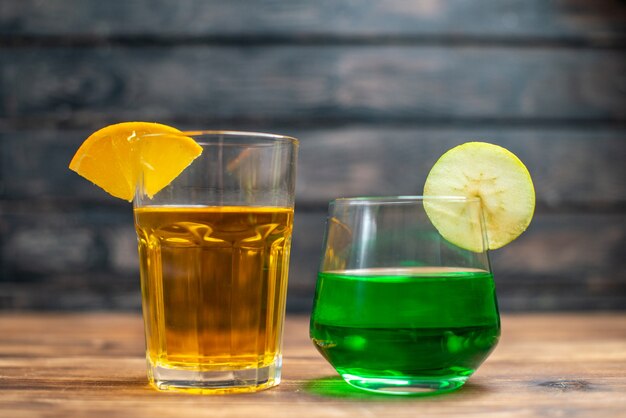 Front view fresh fruity juice orange and apple drinks inside glasses on brown wooden desk