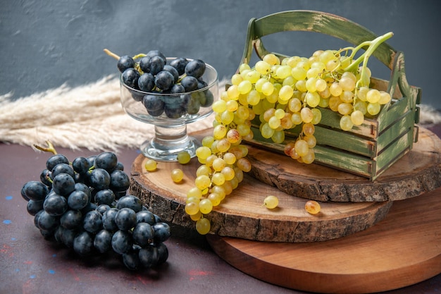Вид спереди свежий виноград зеленые и черные фрукты на темной поверхности вино виноградные плоды спелые свежие древесные растения