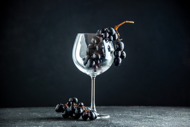 어두운 테이블의 여유 공간에 있는 와인 잔에 있는 신선한 포도 전면 보기