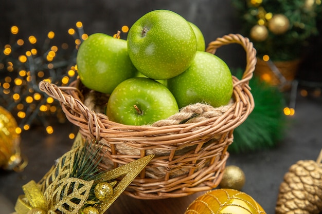 Вид спереди свежие зеленые яблоки вокруг елочных игрушек на темном фоне цветное фото рождественские праздничные фрукты